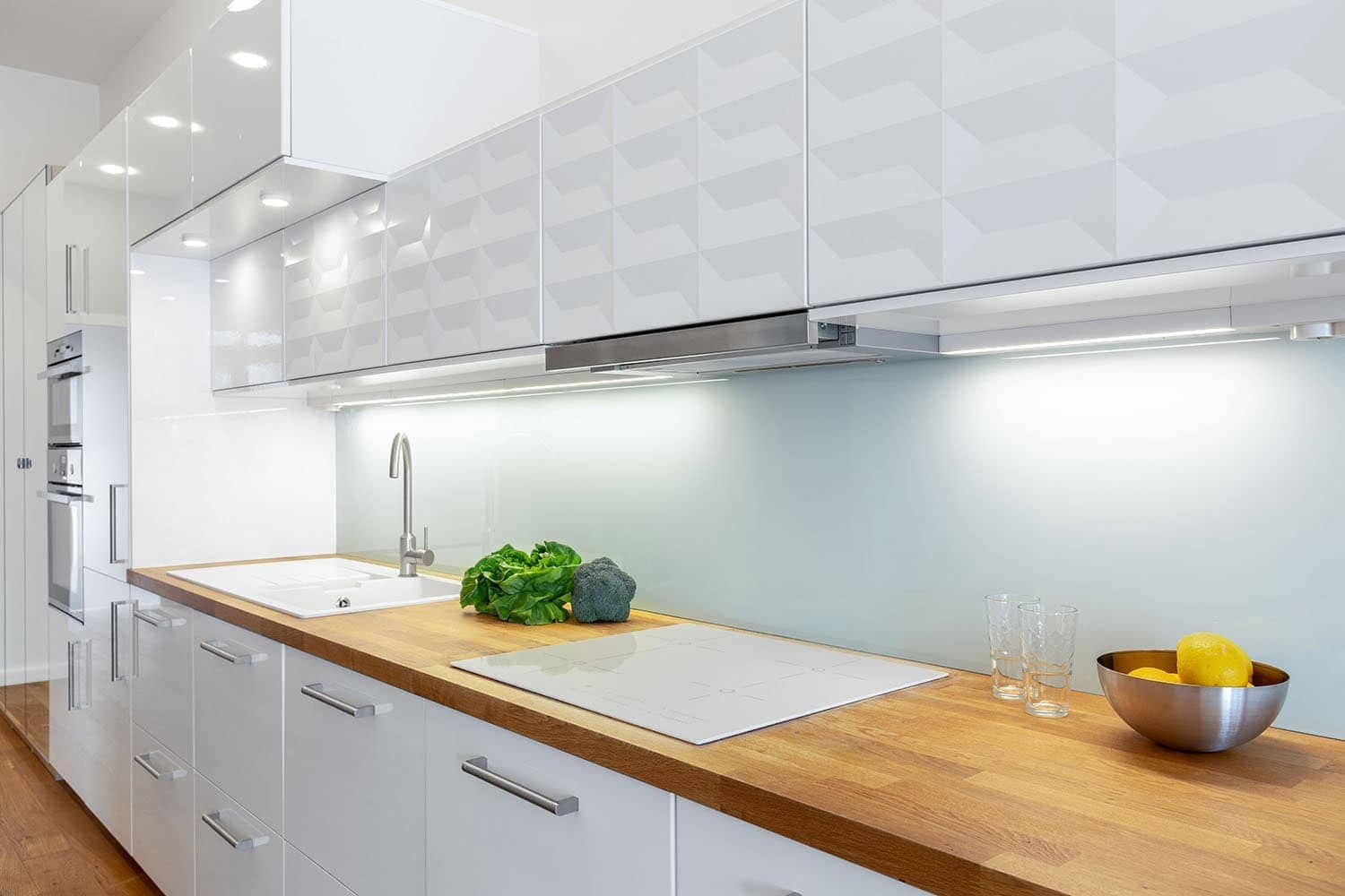 Elegant kitchen with white furniture, wooden countertop and floor and led lights on